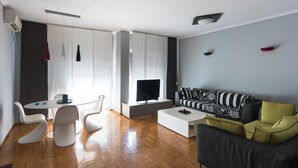 Una sala moderna con televisor de pantalla plana, un sofá, una mesa de centro y un comedor con sillas y una mesa.
