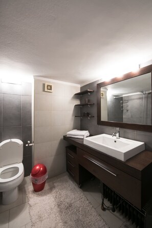 A bathroom with a toilet, a sink, a mirror, and a red trash bin. - Art Maison (Thessaloniki)