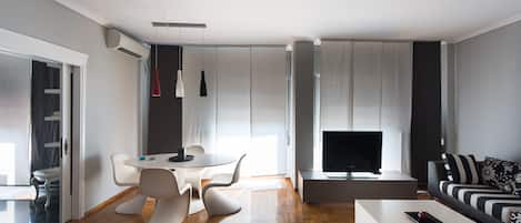 A modern living room with a flat-screen TV, a sofa, a dining table with chairs, and a coffee table.