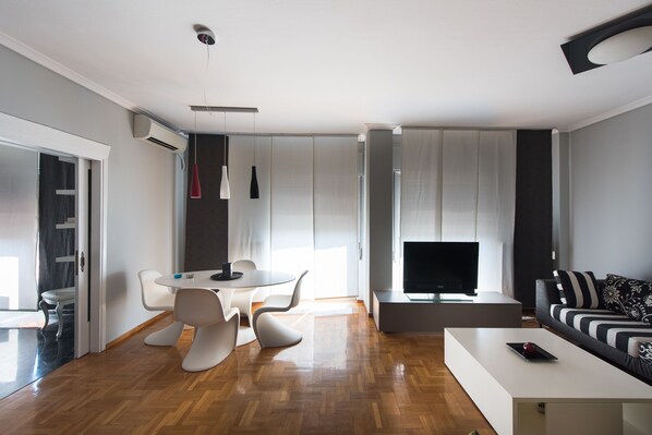 A modern living room with a flat-screen TV, a sofa, a dining table with chairs, and a coffee table. - Art Maison (Thessaloniki)