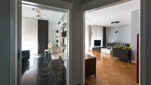 Una sala moderna con sofá, mesa de centro y televisor. Hay un comedor con mesa y sillas. El piso es de madera y las paredes son blancas.