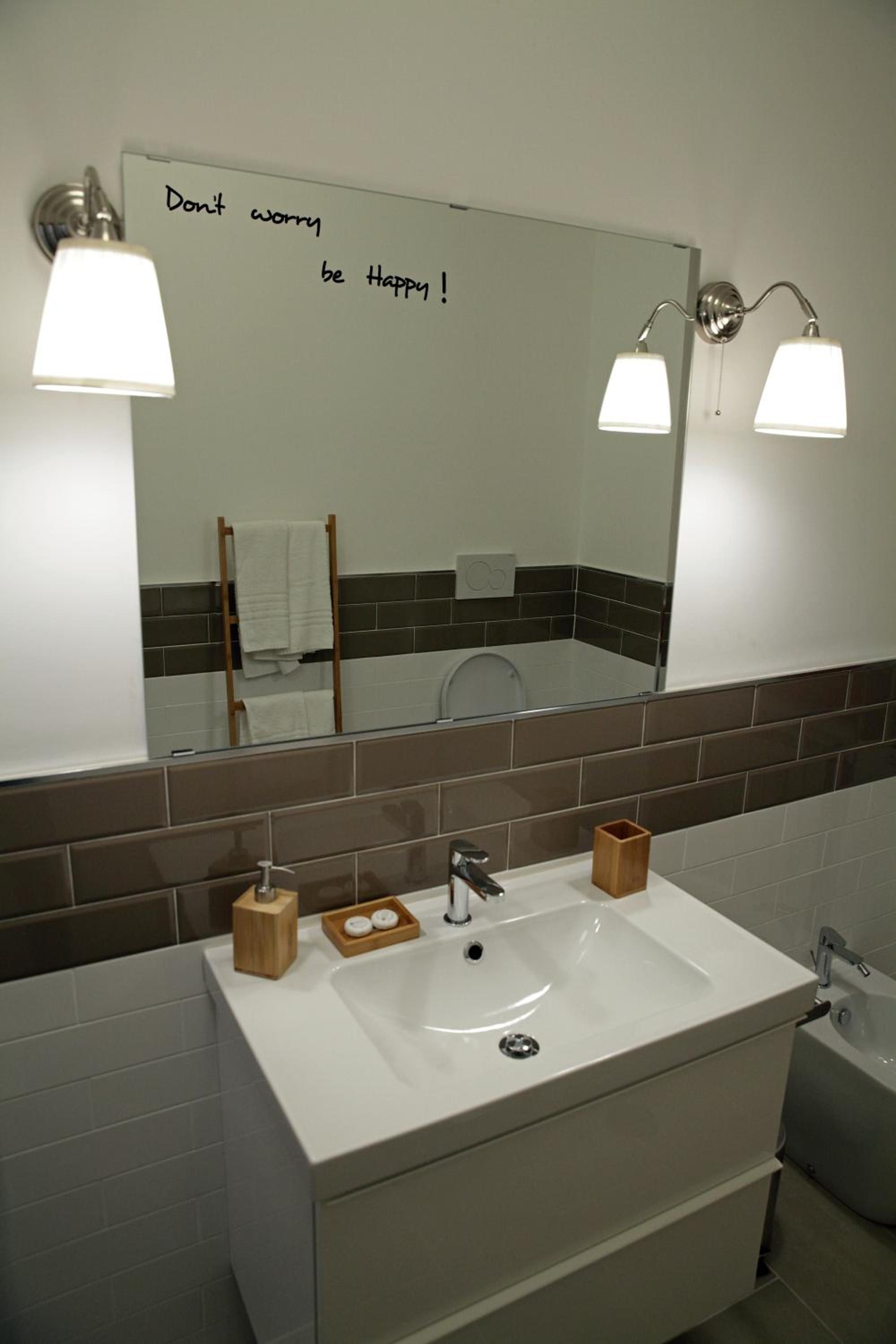 A bathroom with a white sink, two wall-mounted lights, a mirror with a motivational message, and a towel rack.