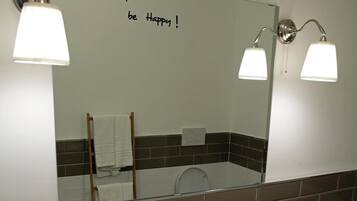 A bathroom with a white sink, two wall-mounted lights, a mirror with a motivational message, and a towel rack.