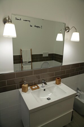Un bagno con un lavandino bianco, due luci a parete, uno specchio con una frase motivazionale e un porta asciugamani.