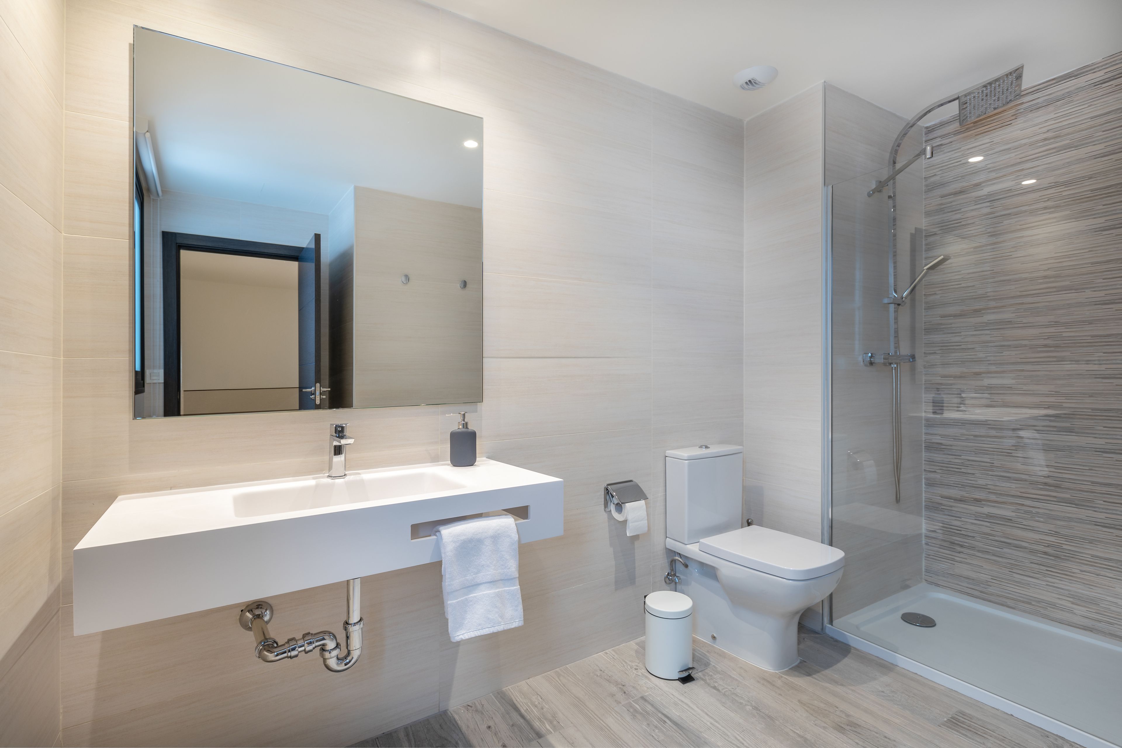 Un baño moderno con lavamanos blanco, espejo, inodoro y cabina de ducha de vidrio.