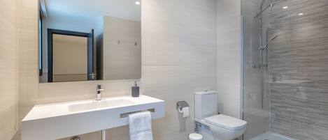 A modern bathroom with a white sink, mirror, toilet, and glass shower enclosure.