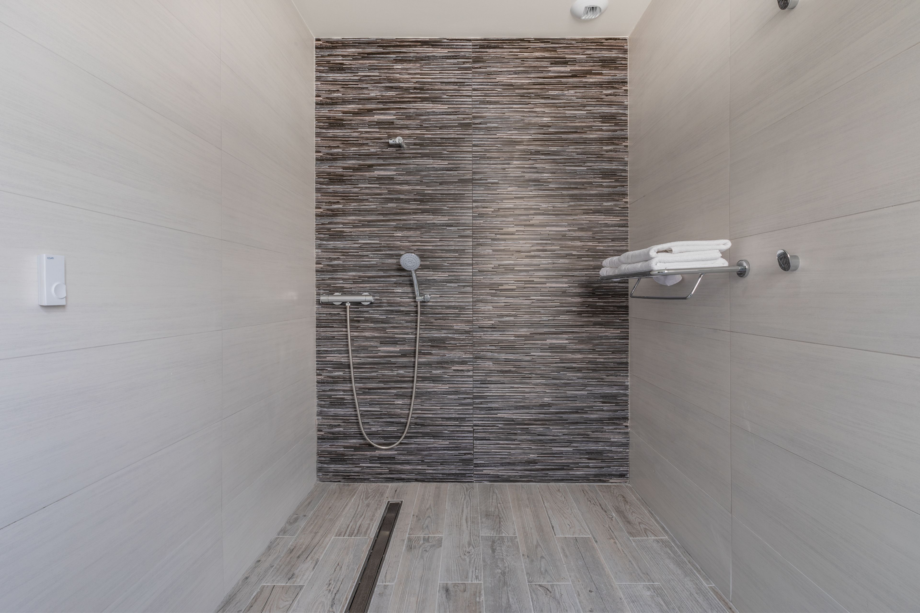 A modern shower with a textured wall, a handheld showerhead, and a towel rack with folded towels.