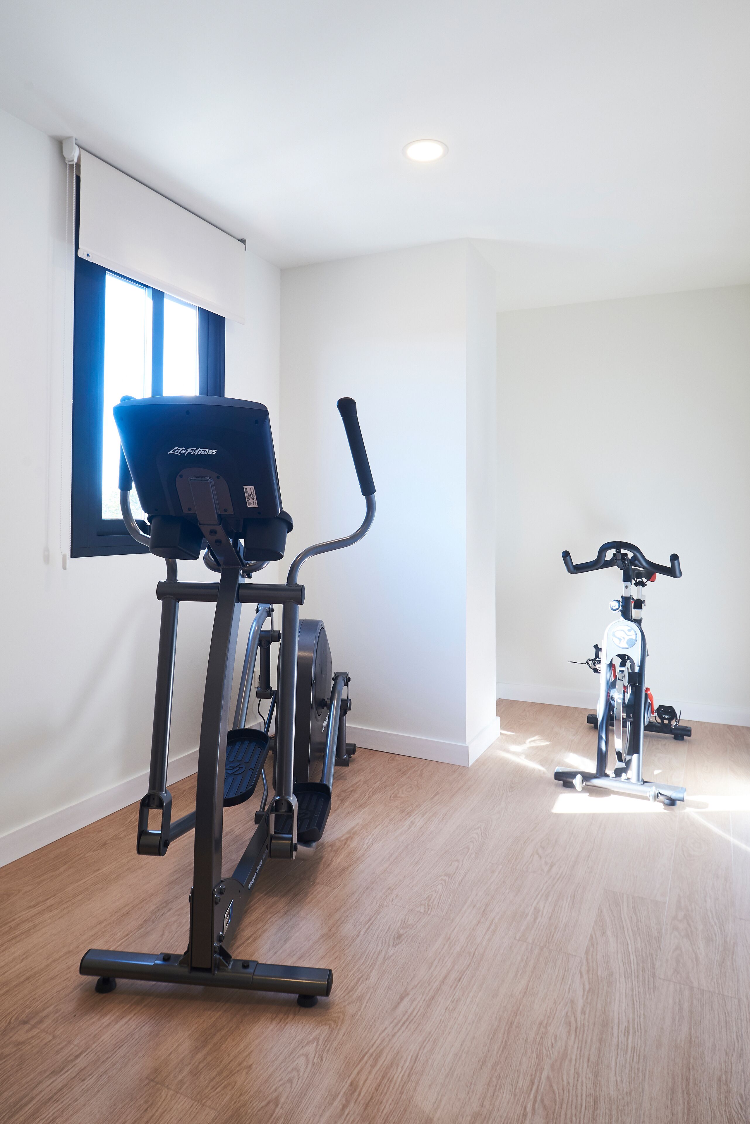 A room with a stationary bike, a treadmill, and a window with blinds.