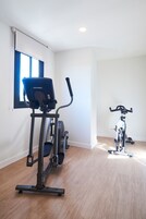 A room with a stationary bike, a treadmill, and a window with blinds.