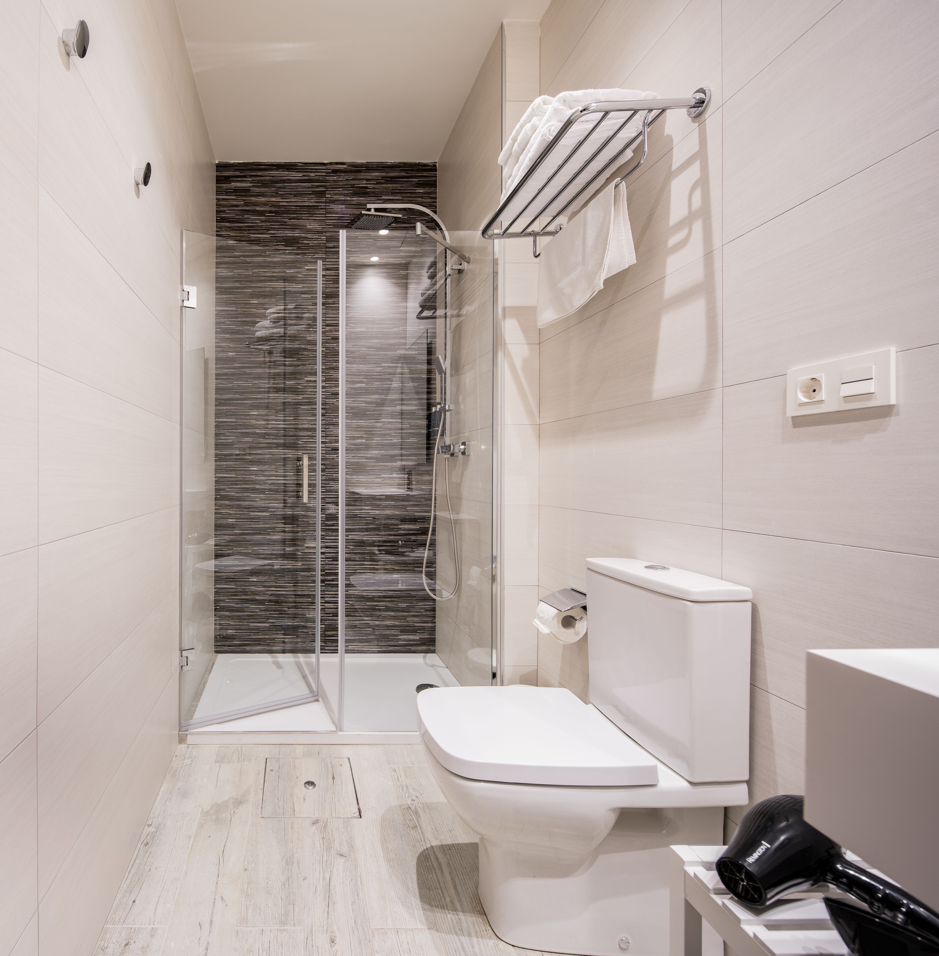Un baño moderno con ducha envuelta en vidrio, inodoro y secador de pelo sobre una encimera.