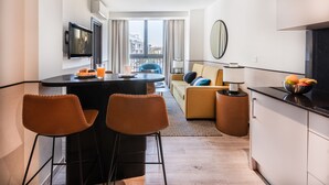 A modern hotel room with a dining area, a sofa, a TV, and a view of the city. - Slow Suites Setas (Seville)
