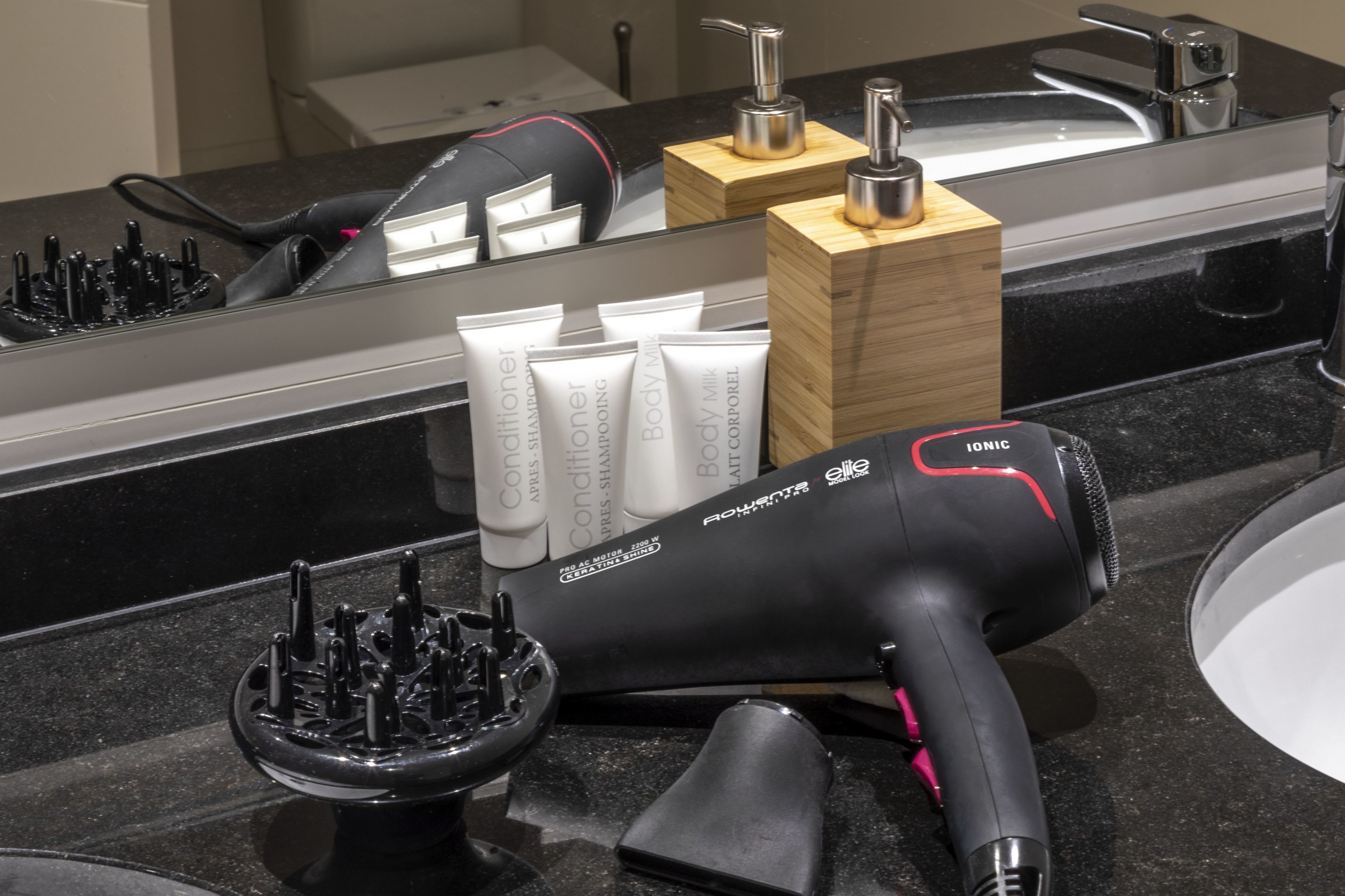 A bathroom vanity with a black countertop, a hairdryer, and a set of toiletries.