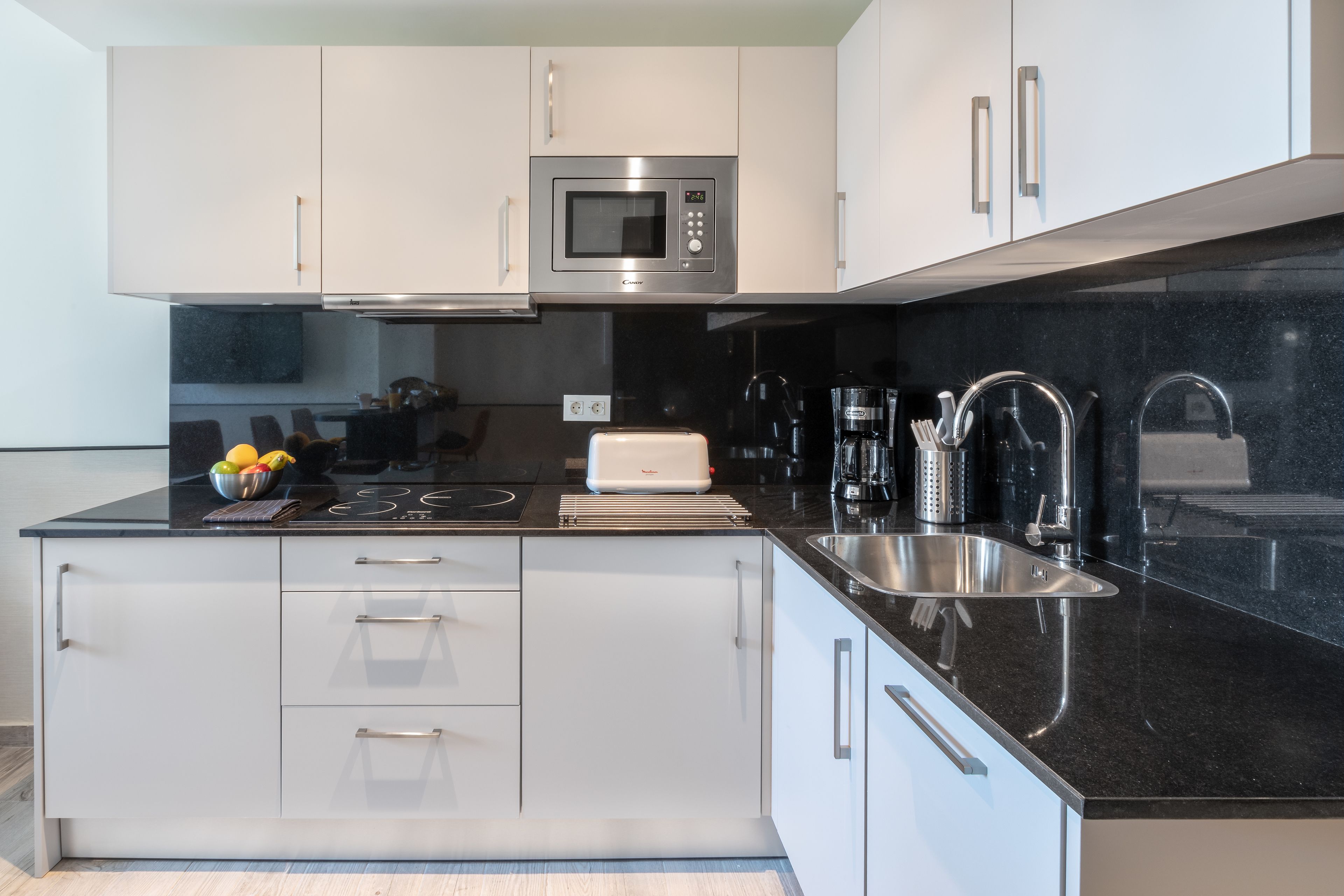 A modern kitchen with white cabinets, a black countertop, a built-in microwave, a toaster, and a sink.