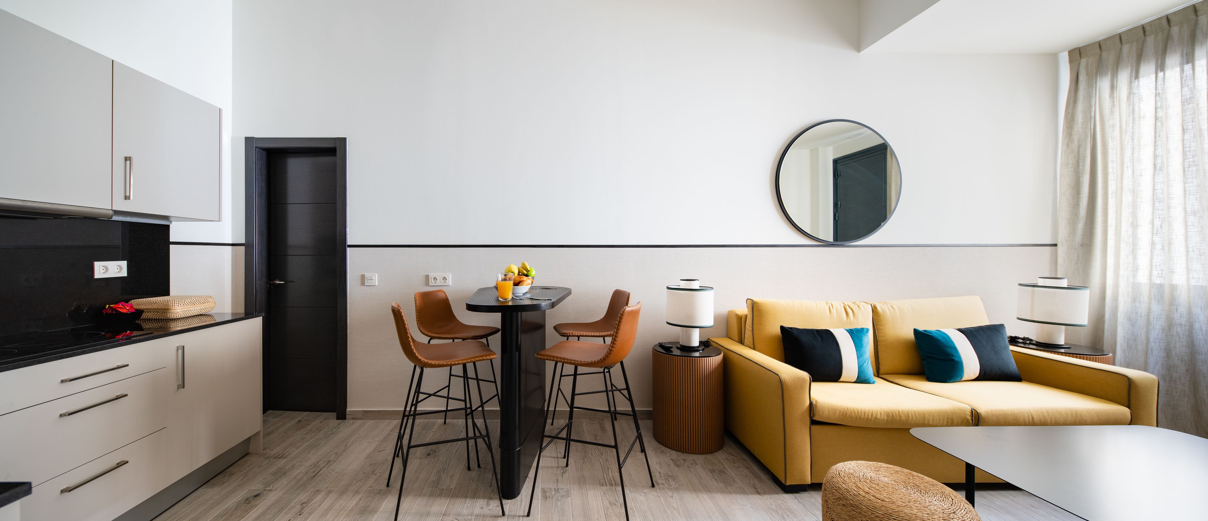 A modern kitchen with a dining area, a sofa, and a round mirror on the wall.