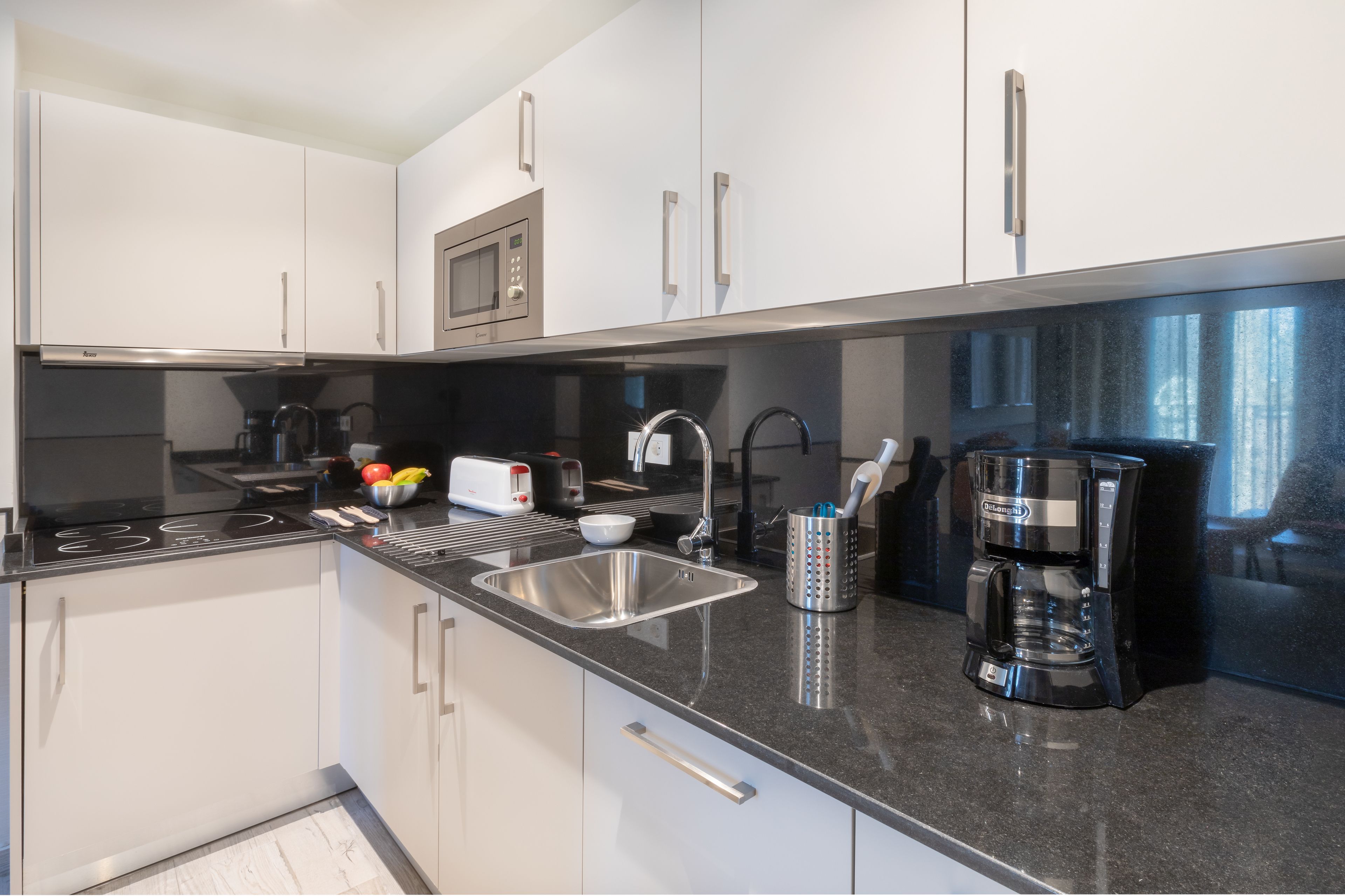 A modern kitchen with white cabinets, stainless steel appliances, a black countertop, and a coffee maker.