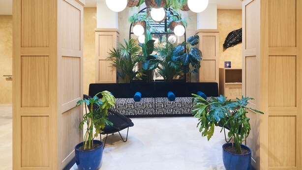A lobby with wooden paneling, a patterned bench, potted plants, and hanging baskets. - Slow Suites Setas (Seville)