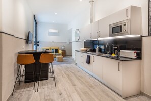 Una cocina moderna con una isla central, taburetes de bar y un microondas.