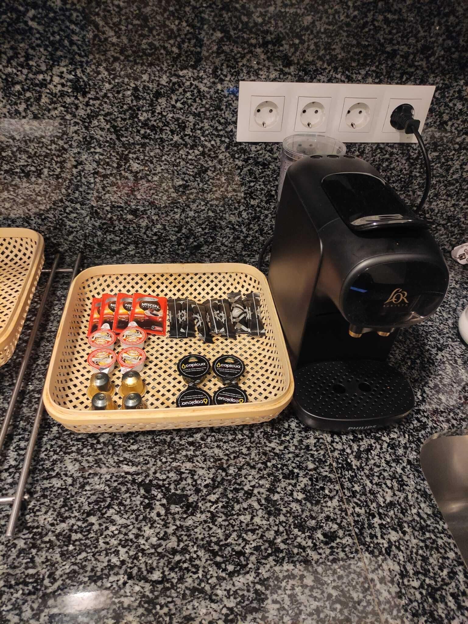 A kitchen counter with a coffee maker, a basket of coffee pods, and a power outlet.