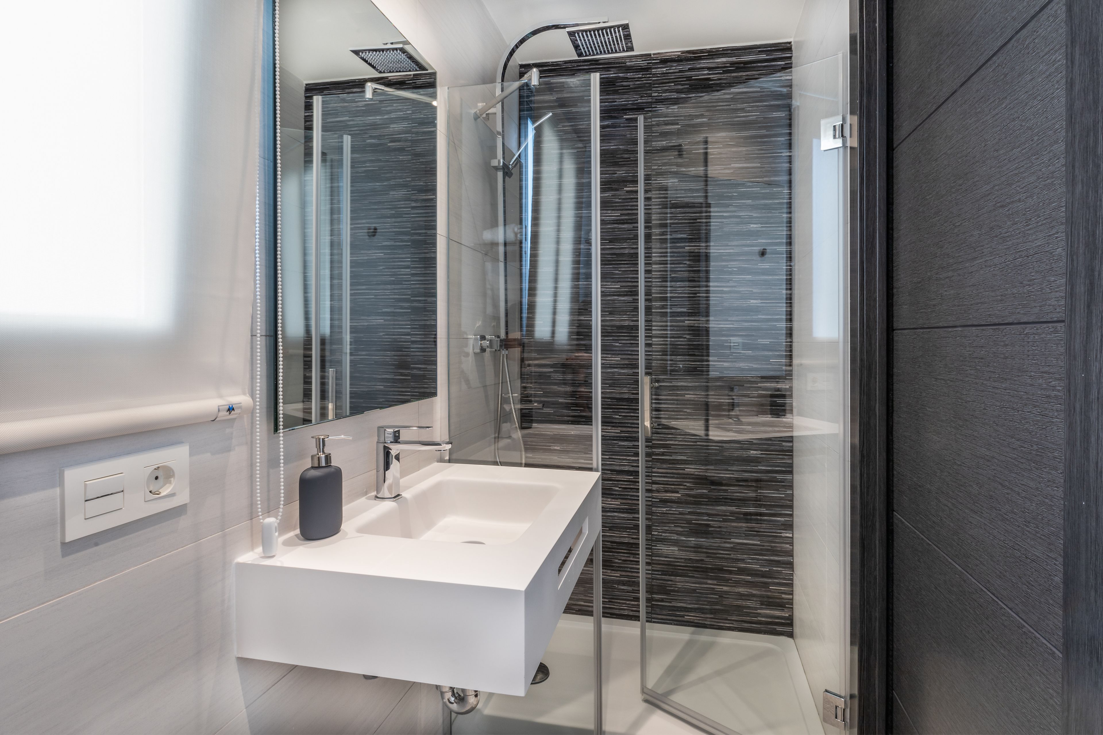 Un baño moderno con cabina de ducha de vidrio, un lavamanos blanco y un espejo.