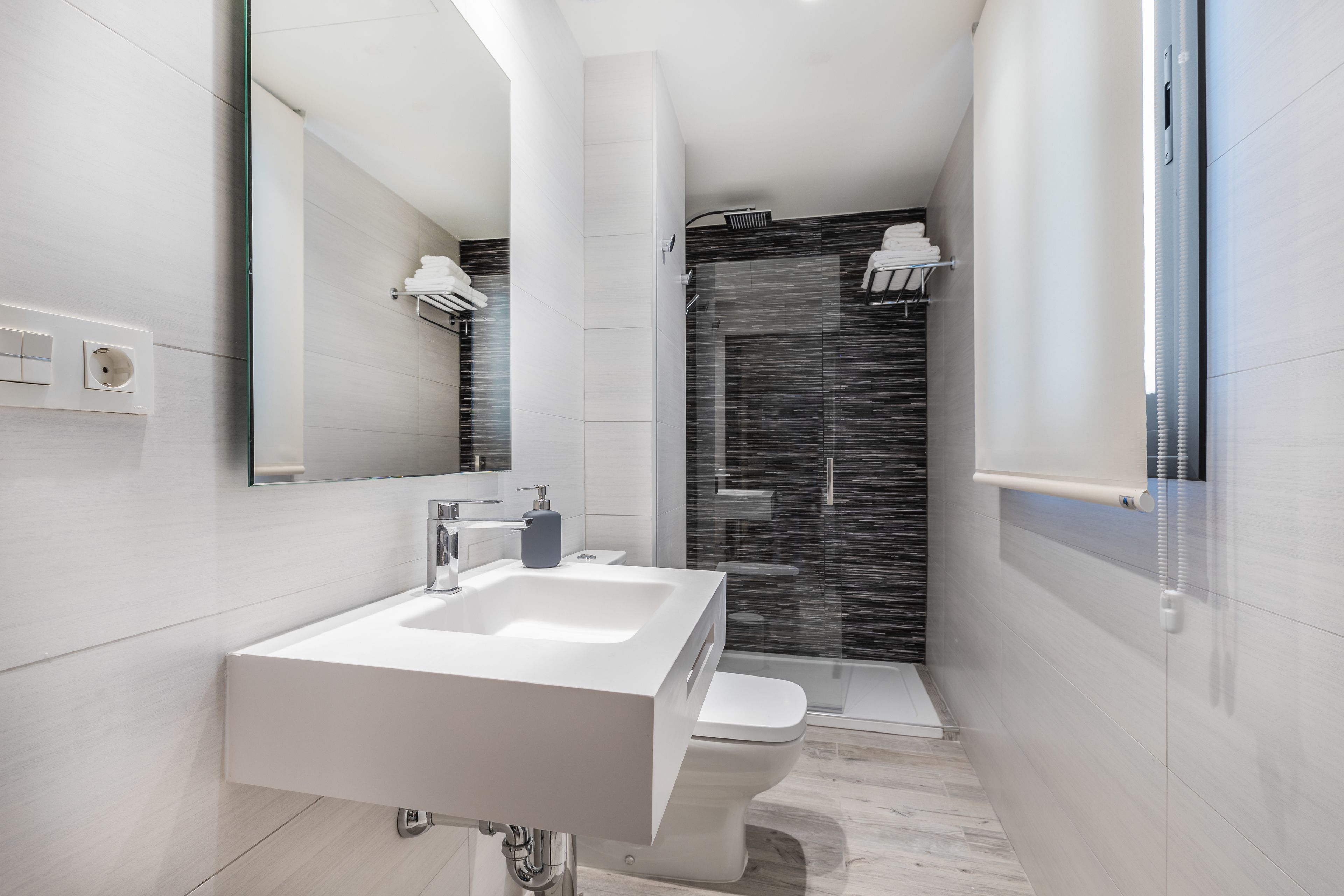 A modern bathroom with a white sink, a toilet, a glass shower enclosure, and a large mirror.