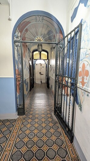 A hallway with patterned flooring, a decorative archway, and a door with a metal gate. - Relais Grand Tour (Florence)