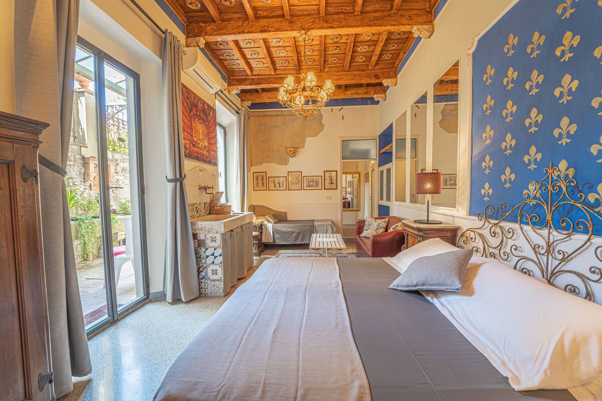 Een slaapkamer met een groot bed, een kroonluchter en uitzicht op buiten.