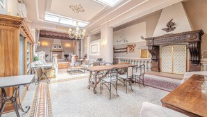 Un comedor espacioso con techo alto, candelabros ornamentales y una gran mesa de madera rodeada de sillas.