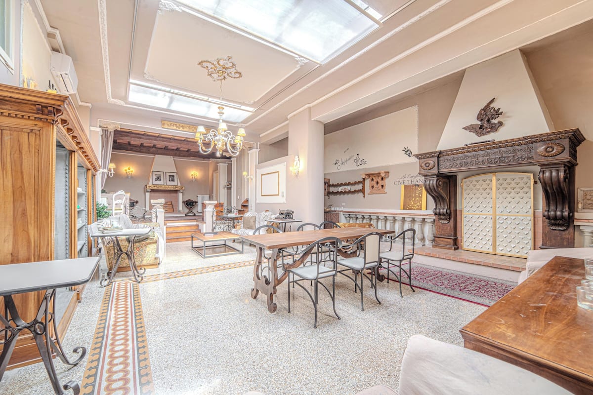 Een ruime eetruimte met een hoge plafond, gedetailleerde kroonluchters en een grote houten tafel omringd door stoelen.