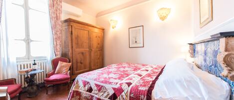 A bedroom with a bed, a wooden wardrobe, a chair, a table, and a window with curtains.