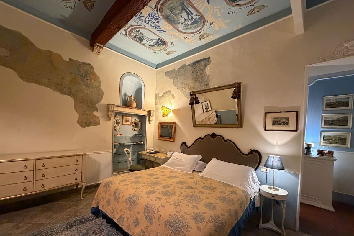 Een slaapkamer met een bed, een kaptafel, een spiegel en een decoratief plafond.
