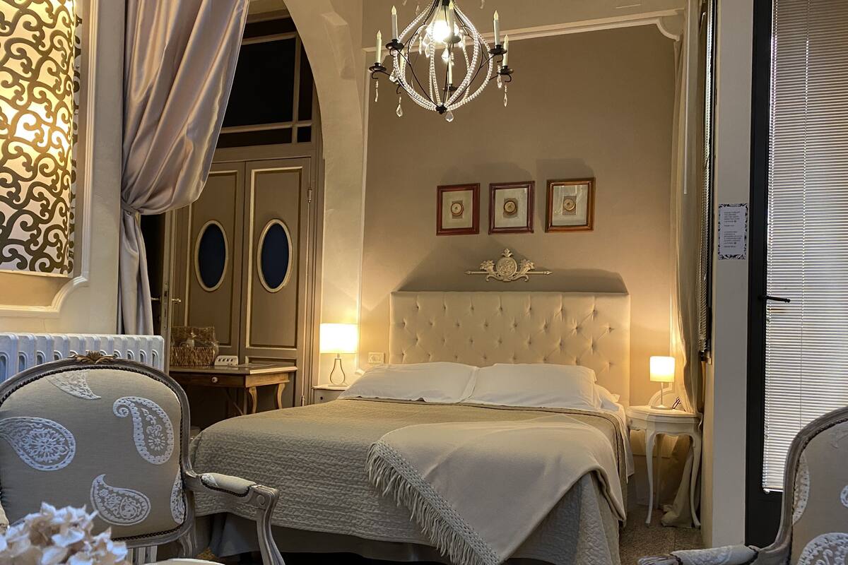 Een hotelkamer met een groot bed, een kroonluchter, een kaptafel met spiegel en een stoel.
