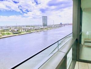 A view from a balcony overlooking a river with modern buildings and a bridge in the distance.