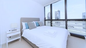 A modern bedroom with a large window, a bed with white bedding, a bedside table, and a lamp. - Brilliant Victoria Harbour Waterfront (Docklands)