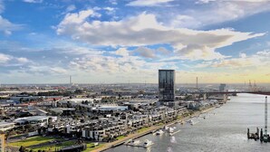 A cityscape with a prominent modern skyscraper, a river with boats, and a bridge in the background. - Brilliant Victoria Harbour Waterfront (Docklands)