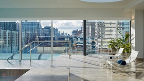 Ruime binnenzone met grote ramen en uitzicht op de stad, een glazen balustrade en enkele comfortabele stoelen.