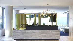 A modern reception desk with a marble top, a large mirror, and a chandelier with multiple spherical lights. - Fawkner Apartment 1B1B (Melbourne)