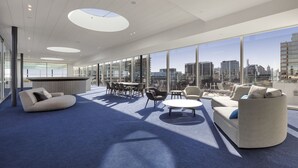 A modern lounge area with a city view, featuring a sofa, chairs, a coffee table, and a bar. - Fawkner Apartment 1B1B (Melbourne)