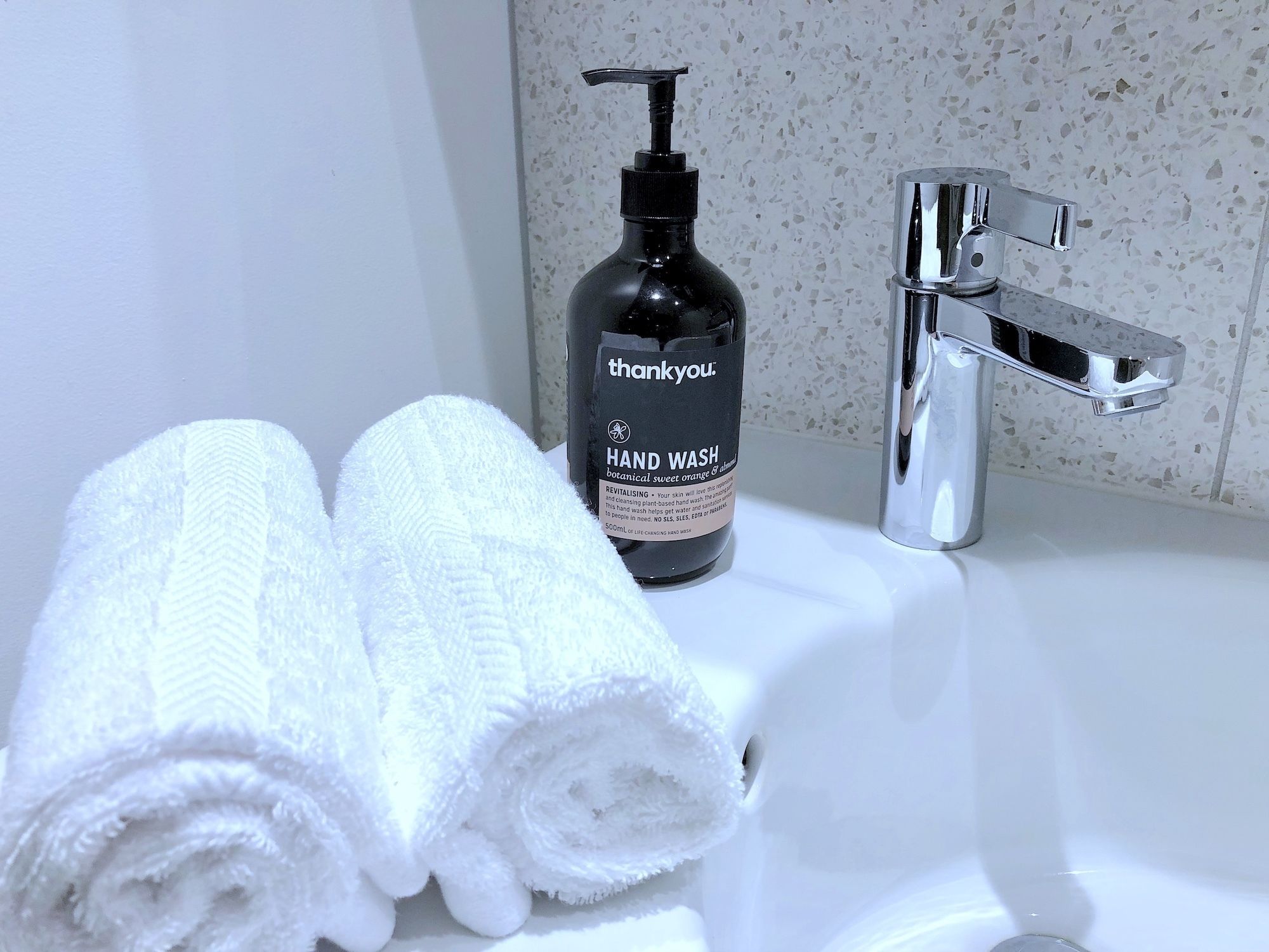 Une salle de bain équipée d’un distributeur de savon liquide, de deux serviettes enroulées et d’un robinet chromé.