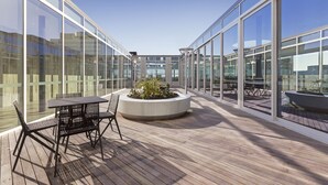 A modern outdoor patio with glass walls, a wooden deck, and a central planter with plants. - Fawkner Apartment 1B1B (Melbourne)