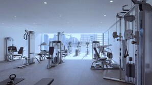 A gym with various exercise machines, a bench, and a view of the city through large windows. - Fawkner Apartment 1B1B (Melbourne)
