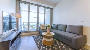 Una sala de estar moderna con un sofá gris, un televisor de pantalla plana sobre un mueble bajo, una mesita de mimbre con un jarrón y una alfombra estampada.