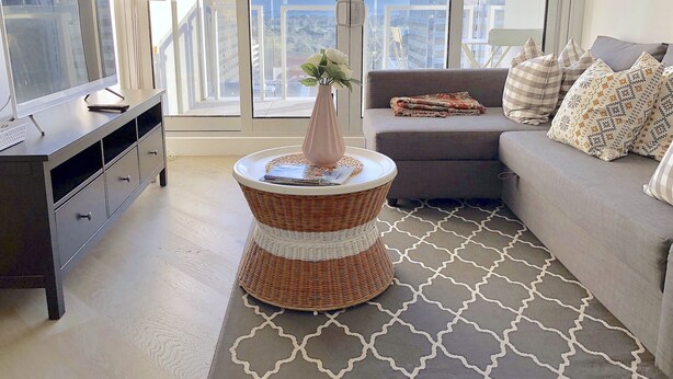A modern living room with a grey sofa, a wicker side table with a vase, and a TV on a dark wooden cabinet. - Fawkner Apartment Bay-view LXI (Melbourne)