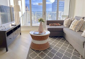 A modern living room with a grey sofa, a wicker side table with a vase, and a TV on a dark wooden cabinet.