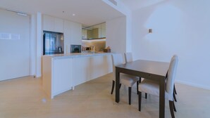 A modern kitchen with white cabinetry, a central island, and a dining area with a dark wooden table and white chairs. - Fawkner Apartment Bay-view LXI (Melbourne)