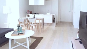 A modern, minimalist living space with a dining area, kitchen, and a flat-screen TV. - Brand New Stunning Home with Garden (Brighton)