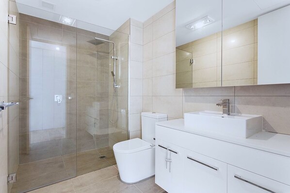 A modern bathroom with a glass-enclosed shower, a white toilet, and a vanity with a mirror.