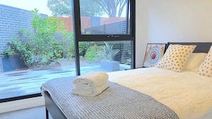A modern bedroom with a large bed, a view of the outdoors, and a window with blinds.