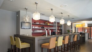Un espace bar doté de nombreux tabourets, d’un téléviseur fixé au mur, et de diverses bouteilles et verres disposés sur des étagères.