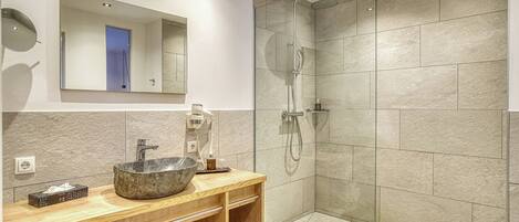 Une salle de bain moderne avec un lavabo en pierre, un meuble-lavabo en bois et une douche à parois de verre.