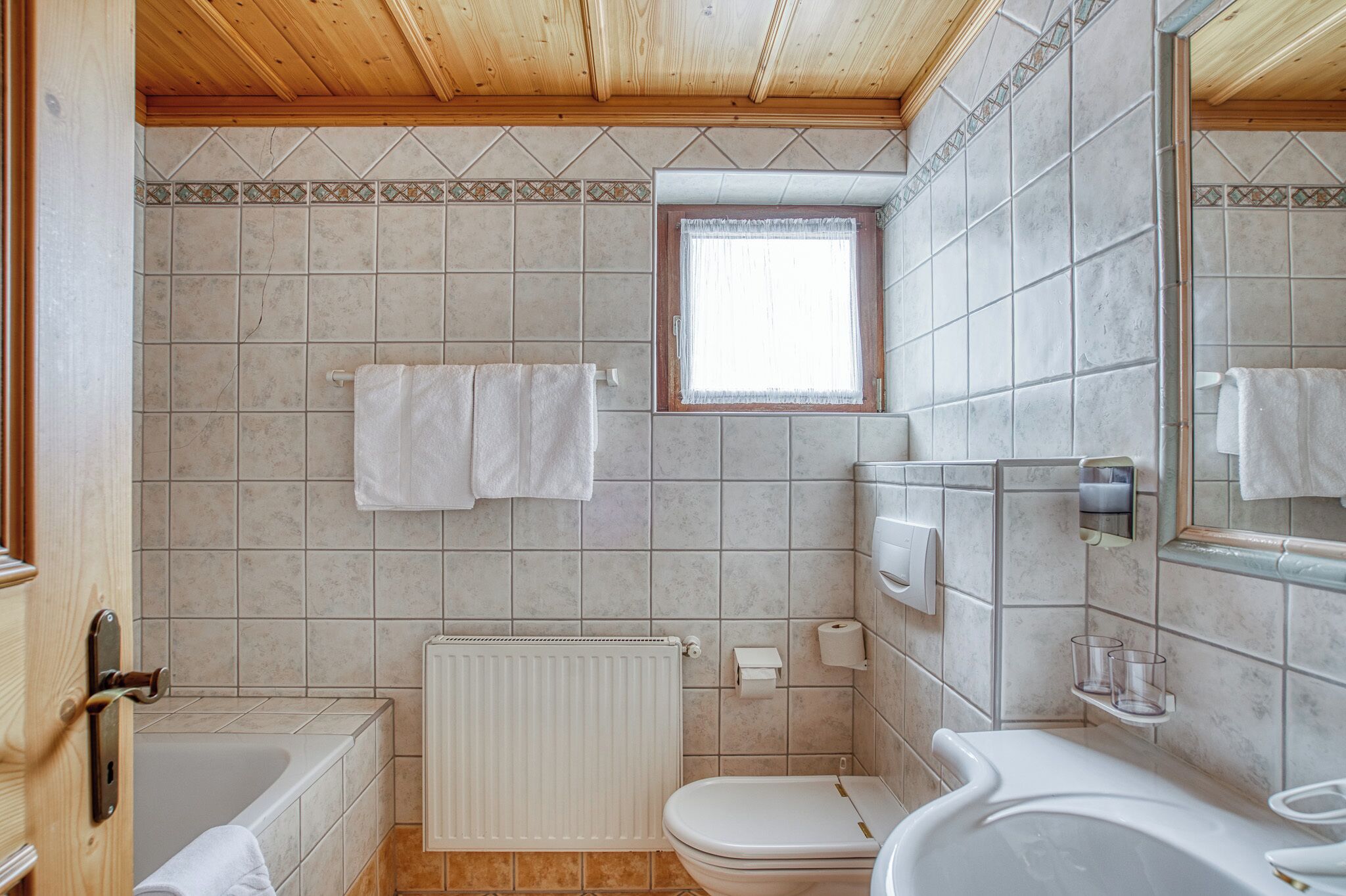 Un baño con bañera, inodoro y lavamanos. Hay toallas colgadas en la pared y una ventana sobre el inodoro.